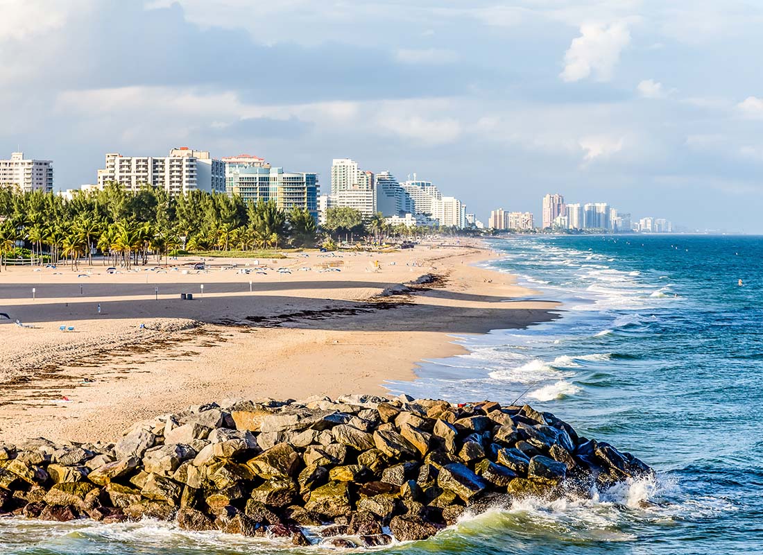 North Ft. Lauderdale, FL - Scenic View of Rocks on a Sandy Beach in North Ft. Lauderdale Florida with Views of Commercial Buildings in the Distance