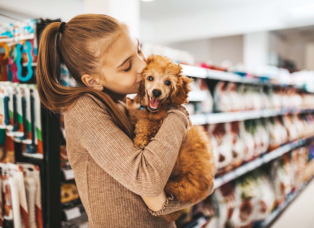 Pet Commercial Insurance - Young and Joyful Girl Shopping in a Pet Store with Her New Poodle Puppy and Giving Him with a Kiss