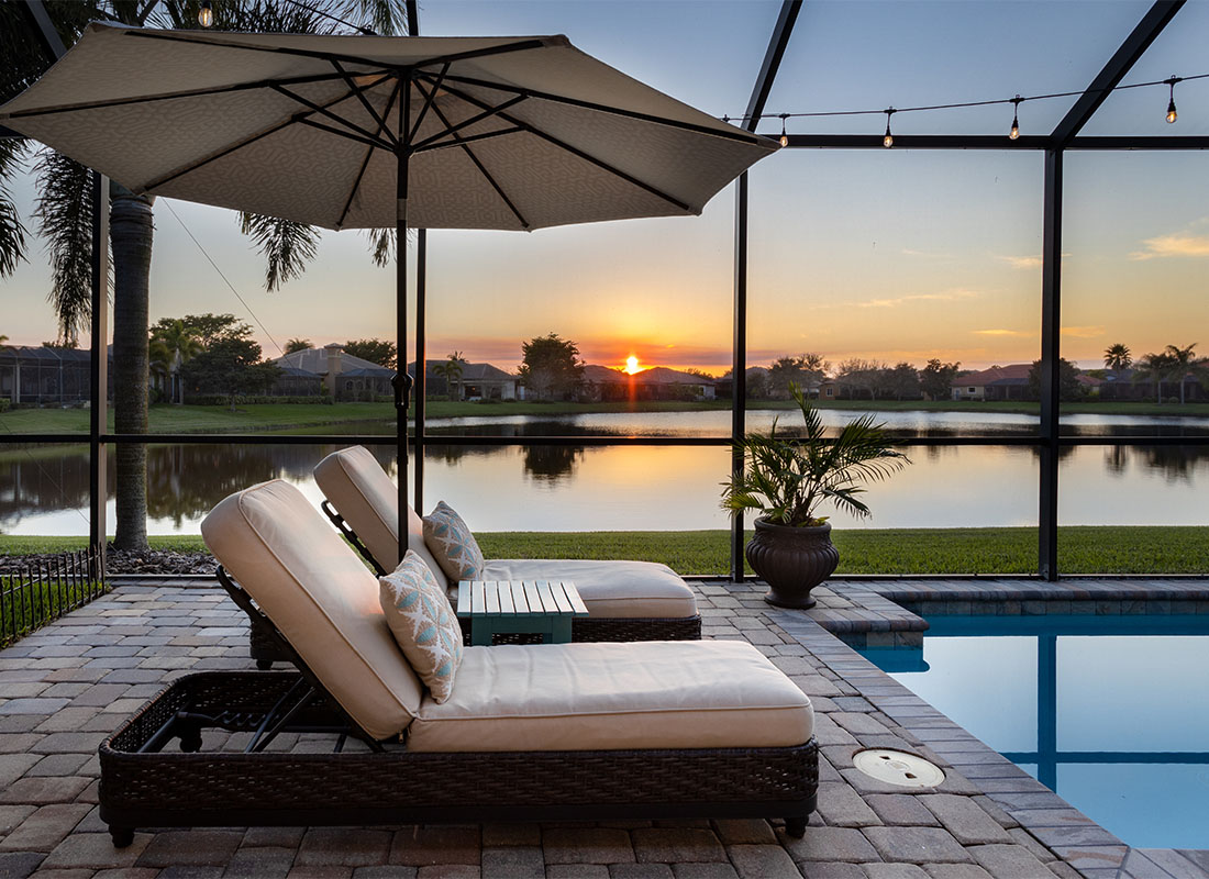 Insurance Solutions - View of Two Lounge Chairs in Between an Umbrella by an Indoor Pool in a Glass Room with Views of the Bay Surrounded by Other Homes at Sunset in Florida