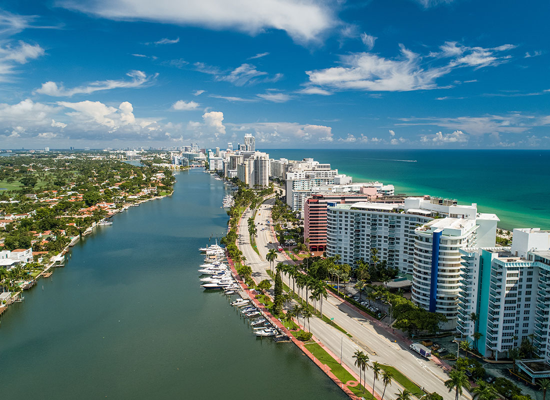 Our Founders Story - Aerial View of Multi Story Buildings Next to the Coast Surrounded by Palm Trees on a Sunny Day in Miami Florida