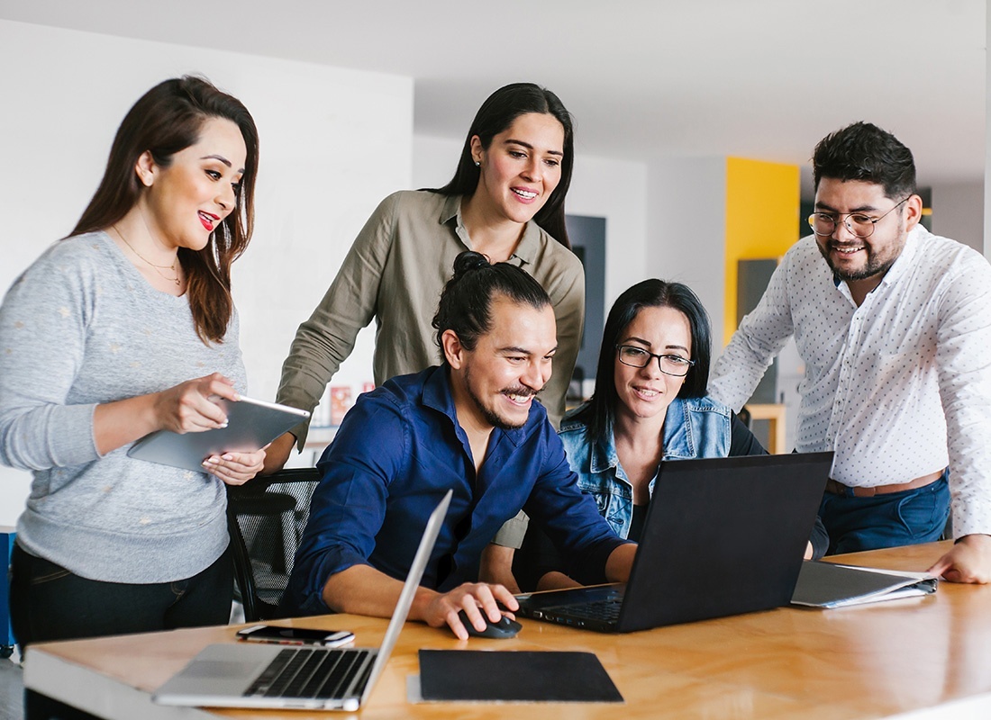 About Our Agency - Team of Smiling Hispanic Employees Working Together on a Laptop Inside a Modern Office